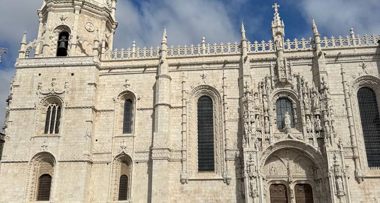 Fachada de piedra clara del ornado Monasterio de los Jerónimos con arcos góticos y altas ventanas contra un cielo azul.