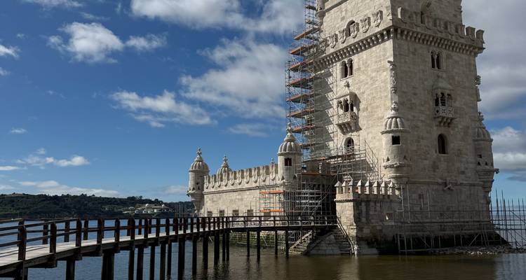 La Torre de Belém elevándose junto al río Tejo, parcialmente cubierta con andamios de restauración en un día soleado.
