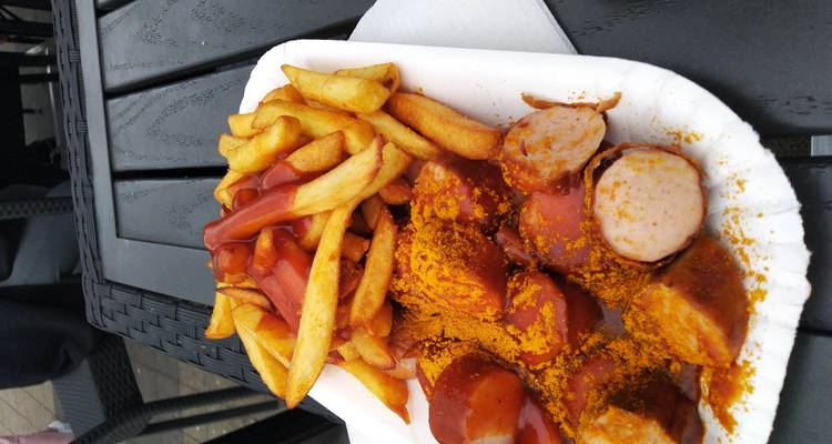 Assiette de currywurst avec frites recouvertes de ketchup sur une table extérieure