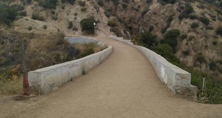 Sentier de randonnée poussiéreux avec de bas murs en pierre sinuant à travers des collines arides