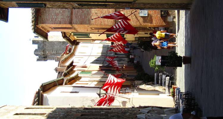 Ruelle médiévale étroite bordée de drapeaux rouges et blancs menant à la porte de la tour en pierre