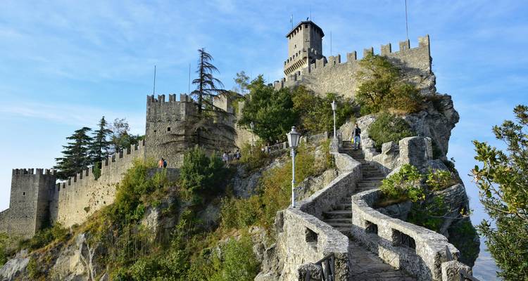 Forteresse de pierre médiévale perchée sur une crête rocheuse avec un escalier d'accès et des visiteurs en exploration