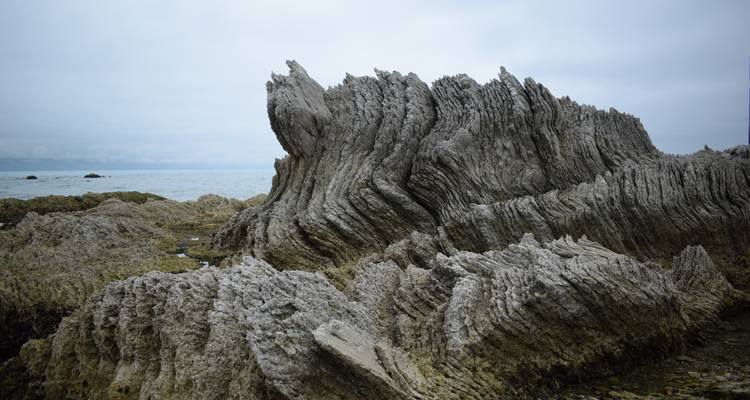 Des rochers calcaires aux formes tourmentées et dentelées surgissent vers la mer sous un ciel gris.