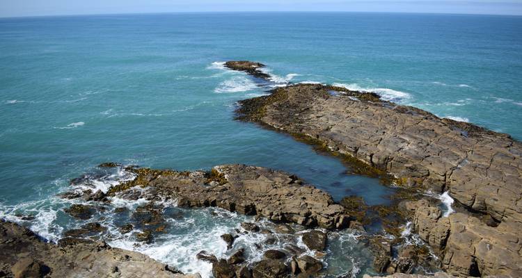Les vagues de l'océan turquoise s'écrasent contre une plateforme rocheuse accidentée et jonchée de varech.