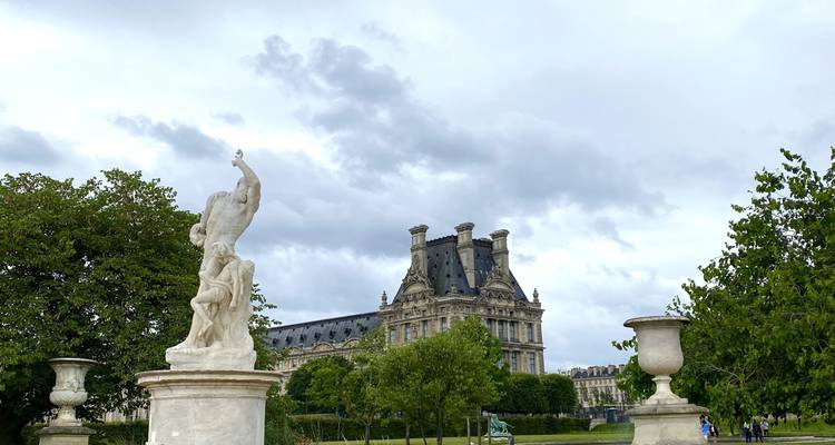 Une sculpture de jardin en marbre se dresse devant le toit du palais historique du Louvre sous un ciel menaçant.