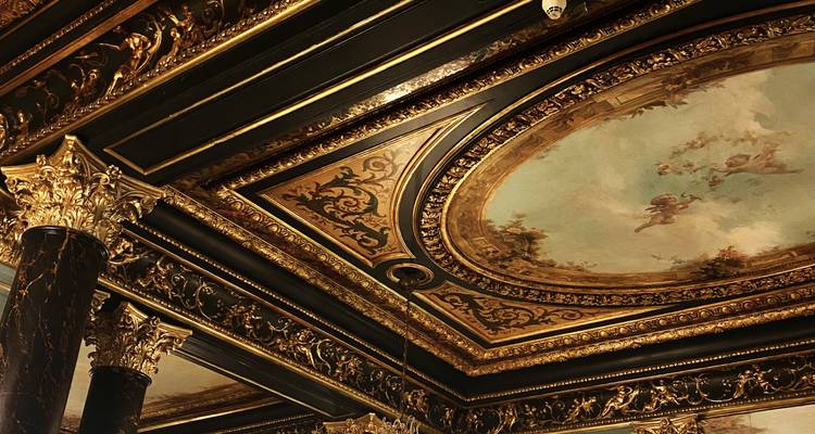 Un plafond richement doré orné de fresques élaborées et de colonnes en marbre noir brille sous une lumière intérieure chaleureuse.