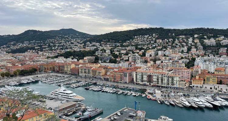 Harbor view of Nice with densely packed buildings climbing the hillside and yachts moored below.