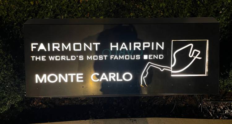 Back-lit sign reading "Fairmont Hairpin – the world's most famous bend – Monte Carlo" photographed at night.