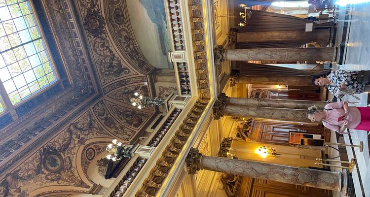 Opulent marble interior with ornate ceiling frescoes and two women admiring the décor.