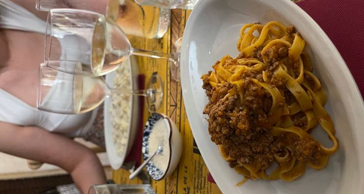 assiette de tagliatelle à la sauce bolognaise avec des verres de vin sur une table de restaurant et deux convives en arrière-plan