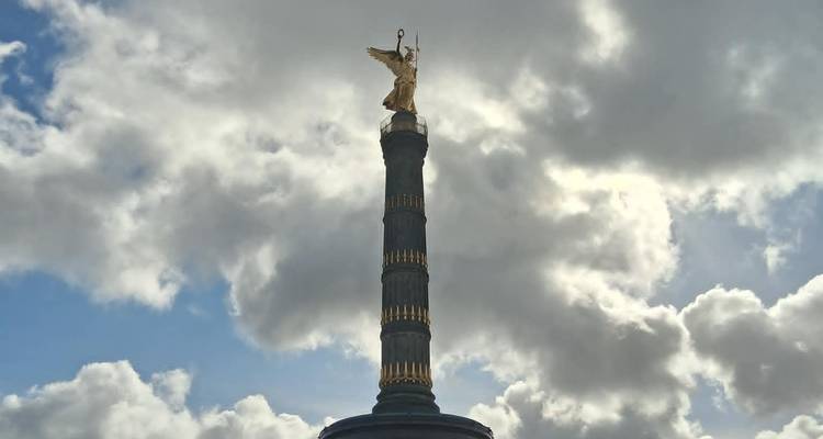 Colonne de la Victoire avec une statue dorée se détachant contre des nuages dramatiques