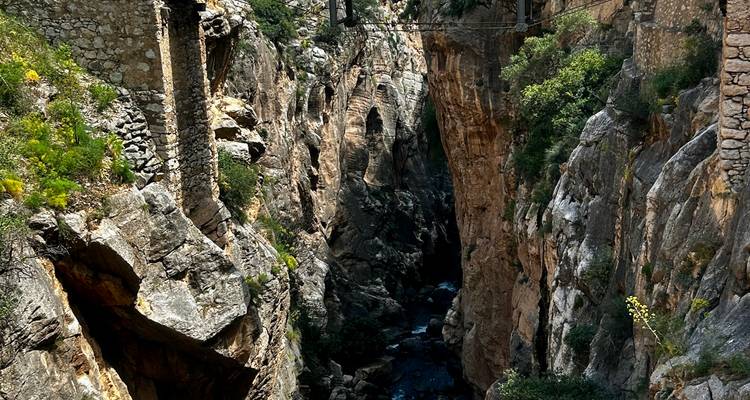A deep rocky gorge with stone pillars, narrow river below, and remnants of an old aqueduct or bridge spanning overhead.