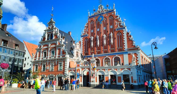 Crowded Old Town square with the ornate House of the Blackheads lit by bright sunshine.