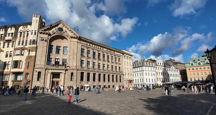 Spacious cobblestone square in Riga Old Town with historic buildings and blue sky with fluffy clouds.