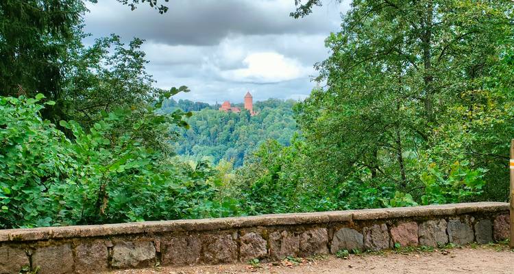 Distant view of red-brick Turaida Castle framed by forested hills, seen from a stone overlook.