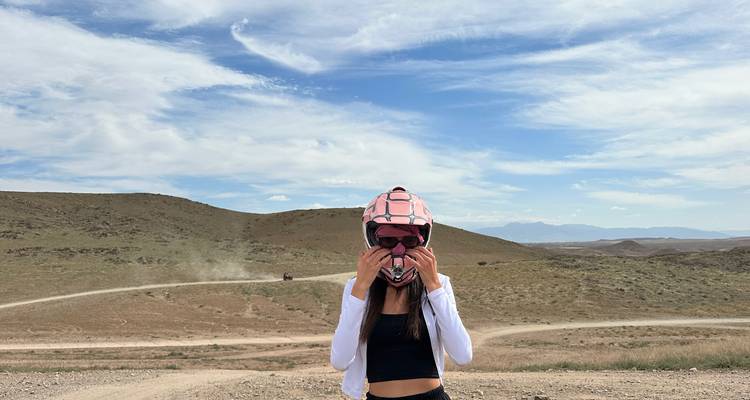 Joven mujer ajustando casco de motocross en terreno desértico abierto bajo cielo azul