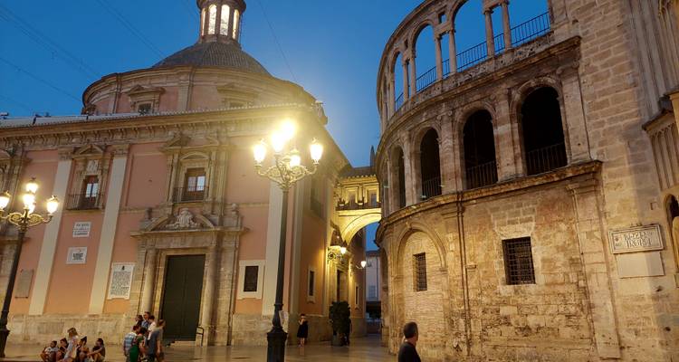 Scène de crépuscule de la Plaza de la Virgen avec des lampadaires doucement illuminés et des façades d'églises historiques.