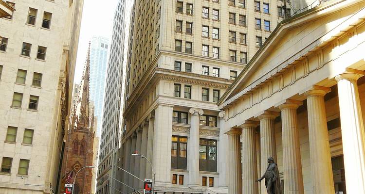 Classic Wall Street scene with historic columns and the statue at Federal Hall flanked by skyscrapers