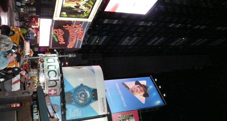Tall vertical view of Times Square billboards glowing at night with crowds and taxis below