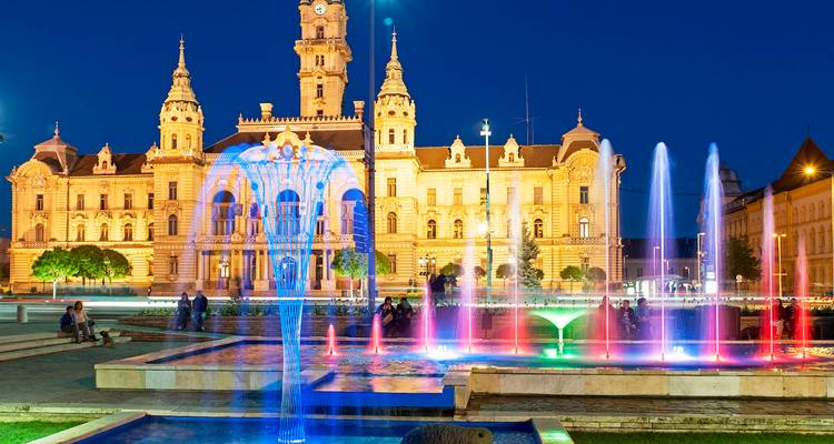 Escena nocturna del ayuntamiento iluminado de Győr con fuentes danzarinas coloridas en primer plano.