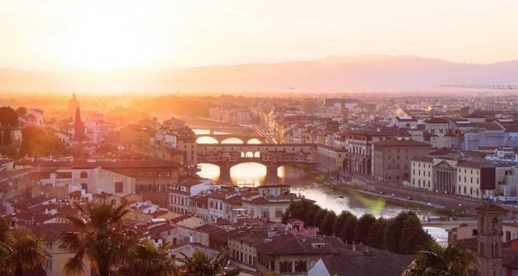 Atardecer dorado sobre Florencia con el Ponte Vecchio y el río Arno brillando bajo un cielo pastel.