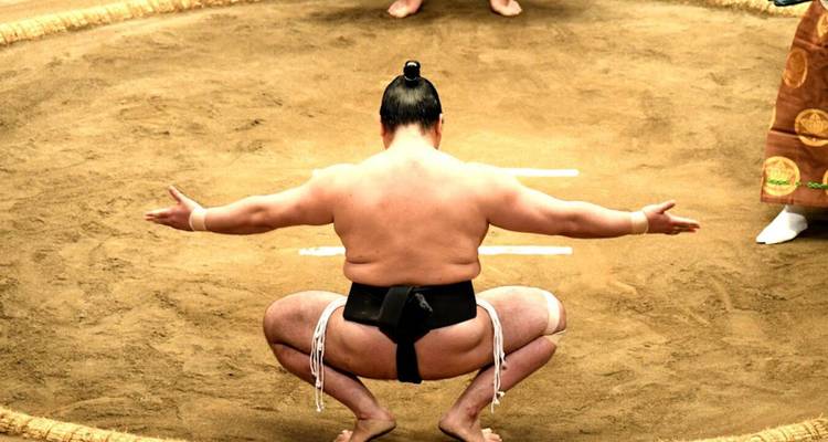 Un lutteur de sumo s'accroupit dans un rituel pré-combat à l'intérieur de l'anneau circulaire du dohyō.