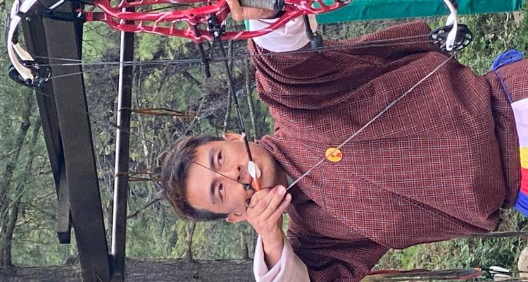Archer bhoutanais en gho traditionnel visant avec un arc à poulies moderne lors d'une compétition