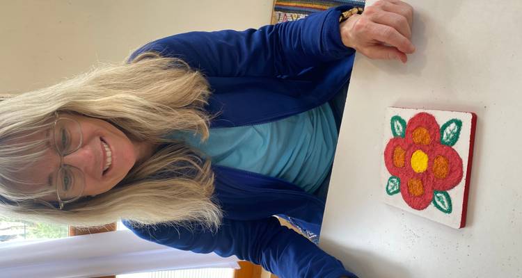 Femme affichant fièrement une tuile de sable et fleurs complétée dans l'atelier