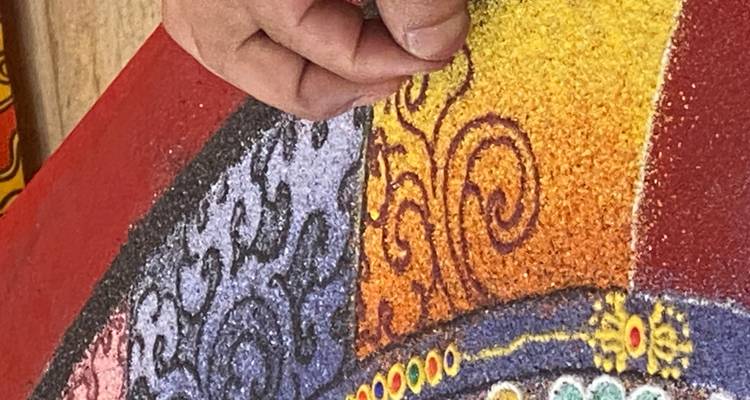 Gros plan d'une main créant un motif complexe de mandala en sable avec des grains de couleur