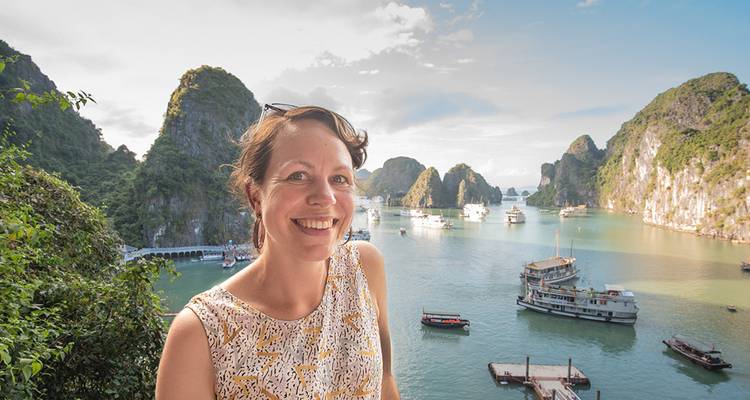 A smiling traveller with karst islands and cruise boats of Halong Bay behind her.