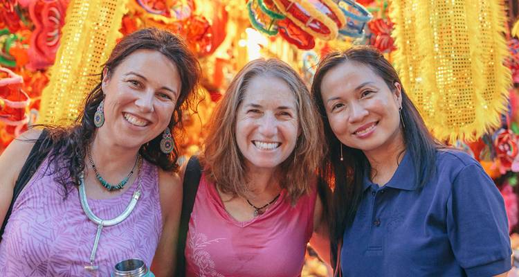 Three women smiling in front of colourful festival lanterns.