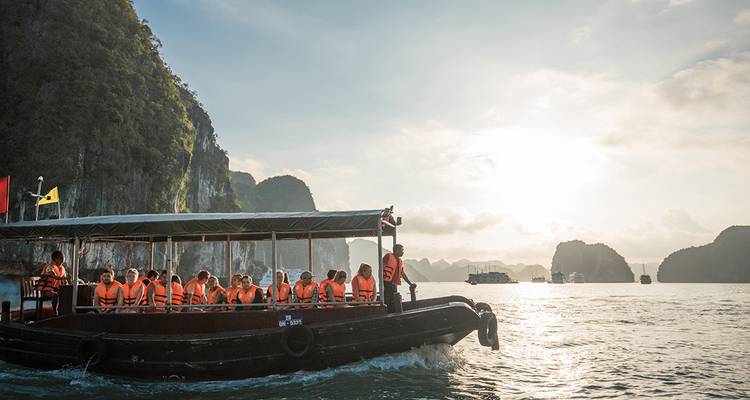 Tourists in lifejackets on a small boat cruising between limestone cliffs at sunset.