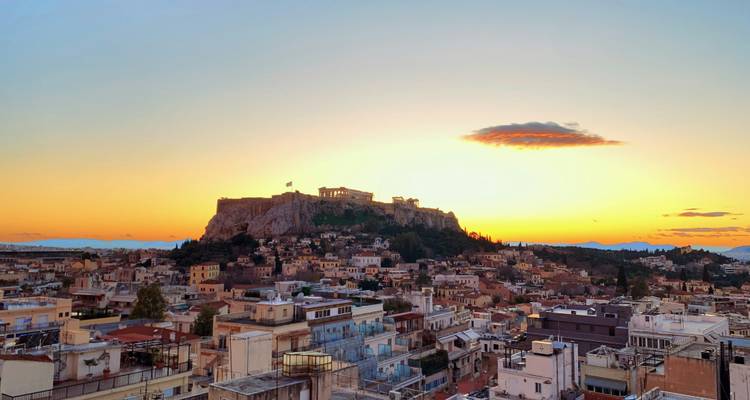 Sunset view over Athens with the Acropolis hill rising above a cityscape of pastel buildings.