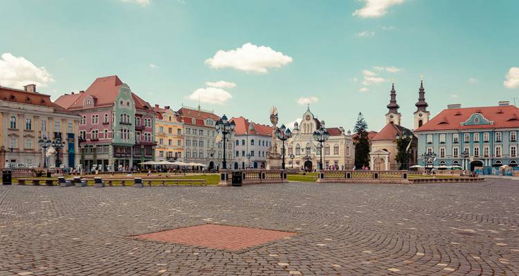 Breiter Kopfsteinplatz umgeben von pastellfarbenen historischen Gebäuden und Kirchtürmen unter blauem Himmel.