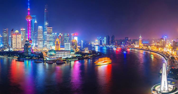 Panorama nocturne vivant de la skyline illuminée de Shanghai se reflétant dans la rivière Huangpu avec les traces lumineuses des bateaux.