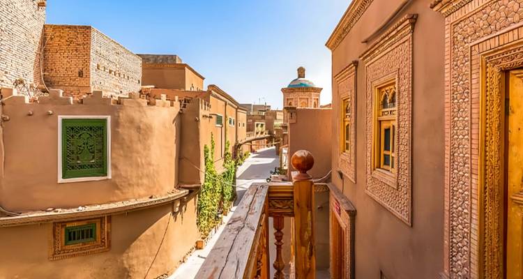 Un callejón brillante e iluminado por el sol bordeado de casas uigures en tonos tierra con ventanas ornamentadas y trabajos en ladrillo en la Ciudad Vieja de Kashgar.
