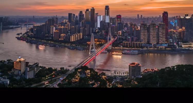 Horizonte al atardecer de Chongqing con un puente colgante iluminado atravesando el río Yangtsé.
