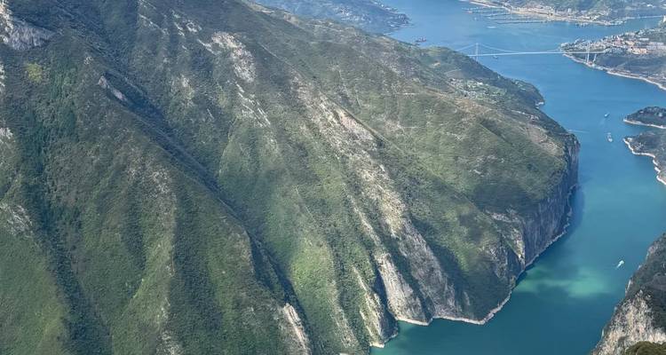 Las paredes del cañón verde y escarpado descienden hacia aguas turquesas estrechas con un puente a lo lejos.
