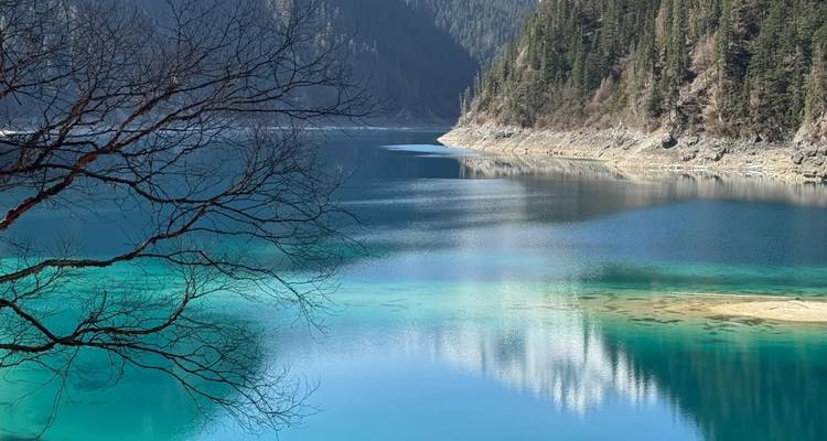 Lago alpino de agua cristalina en Jiuzhaigou que refleja montañas boscosas y el cielo.