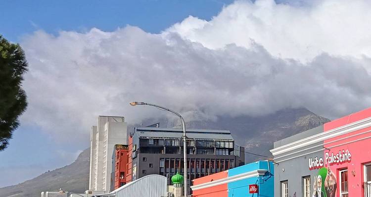 Colorful modern buildings beneath low clouds spilling over a mountain ridge in Cape Town.