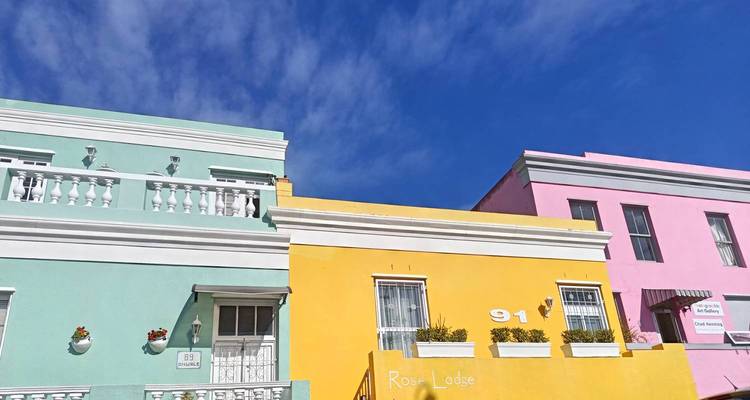 Bright pastel facades of Bo-Kaap houses—mint, yellow and pink—against a vivid blue sky.