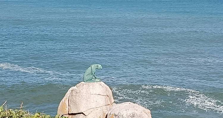 Small green bronze lizard sculpture perched on a seaside boulder with waves below.