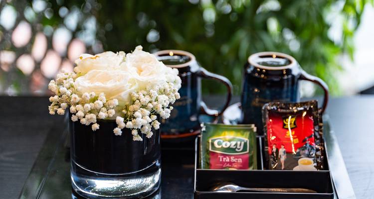 Gros plan d'un plateau avec des roses blanches, des tasses à thé et des sachets de thé assortis disposés sur un fond de verdure feuillue.