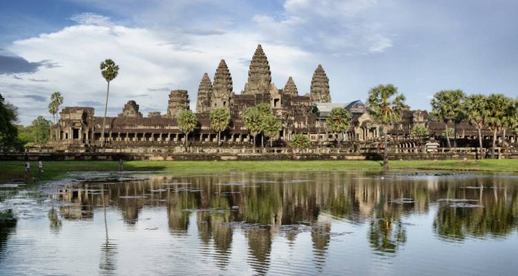 Panoramic view of Angkor Wat temple complex reflected in moat on a bright day.