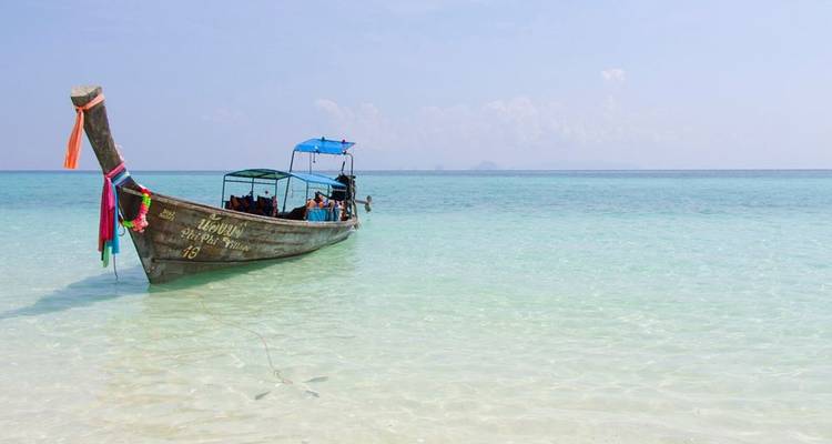 Traditional long-tail boat floating in crystal clear sea with passengers relaxing under canopy.