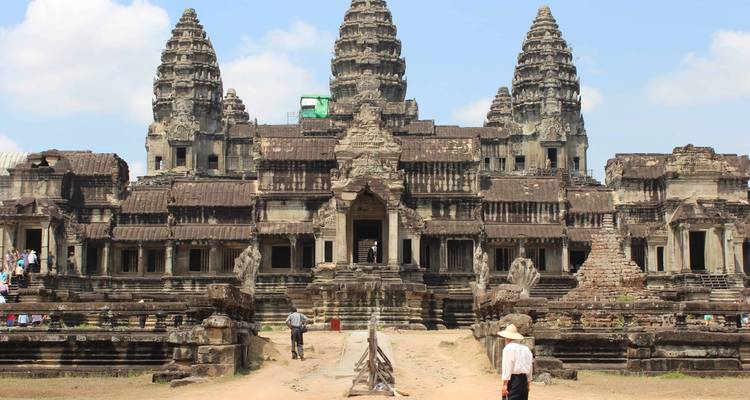 Front façade of Angkor Wat with visitors exploring ancient stone architecture under blue sky.