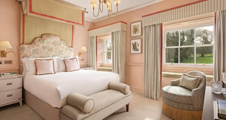 Elegantes Hotelzimmer in Pastelltönen mit Gartenblick, komfortablem Bett und klassischer Einrichtung.