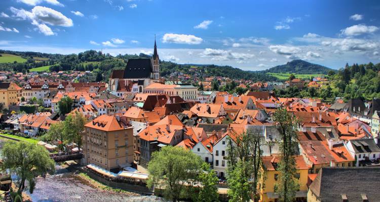 Panoramic view of Cesky Krumlov’s red-roofed town nested in green hills under a bright sky