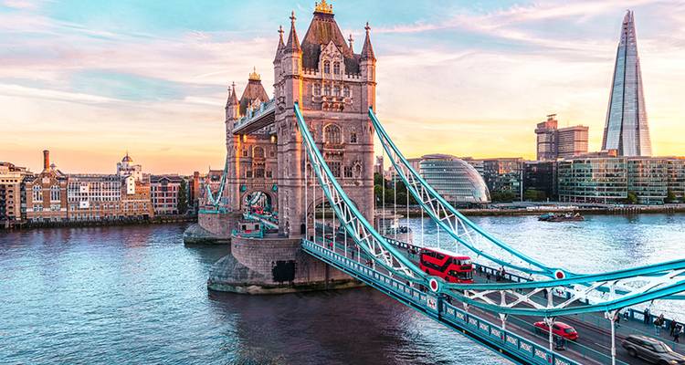 Tower Bridge and the Shard stand over the Thames during a pastel sunset with red double-decker bus crossing.