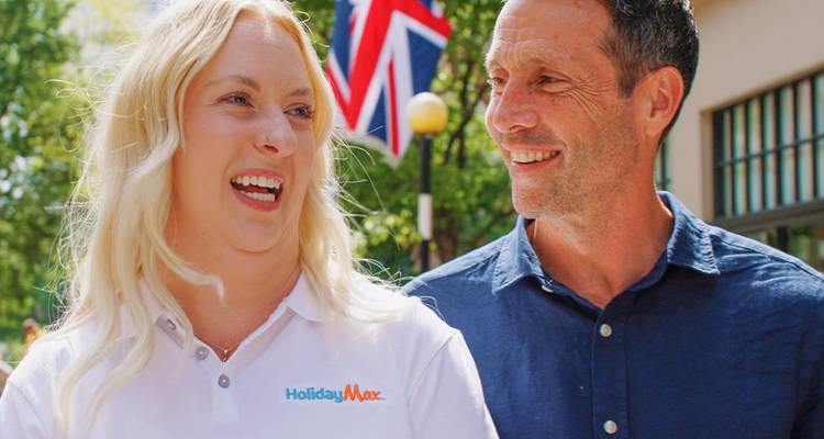 Smiling couple stroll beneath a British flag while on a guided city tour, host wearing HolidayMax shirt.